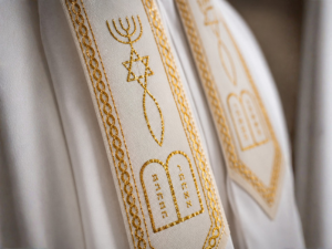 Close-up of The Blessing Tallit collar showing the Menorah, Star of David, Fish symbol, and Ten Commandments tablets embroidered in gold.